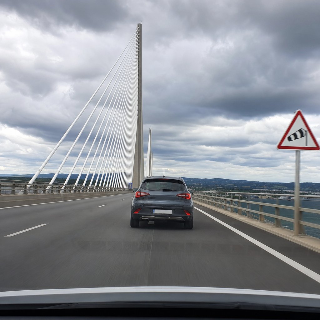 voiture particulière sur un pont exposé à un fort vent latéral, conducteur tenant fermement le volant, trajectoire stable dans sa voie, environnement routier français avec glissières de sécurité